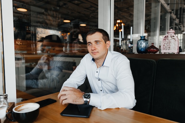 Apuesto joven empresario sonríe y bebe café en un café. hombre de traje con café.