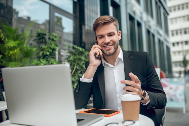 Apuesto joven empresario trabajando en la cafetería y hablando por teléfono