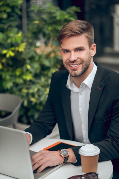 Apuesto joven empresario trabajando en una computadora portátil y sonriendo