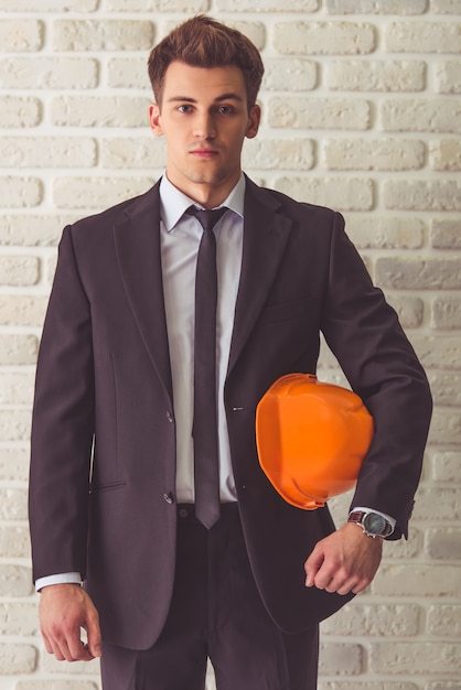 Apuesto joven empresario en traje está sosteniendo un casco.