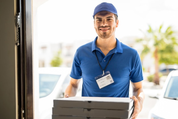 Apuesto joven entregando unas cajas de pizza a la puerta principal con una sonrisa