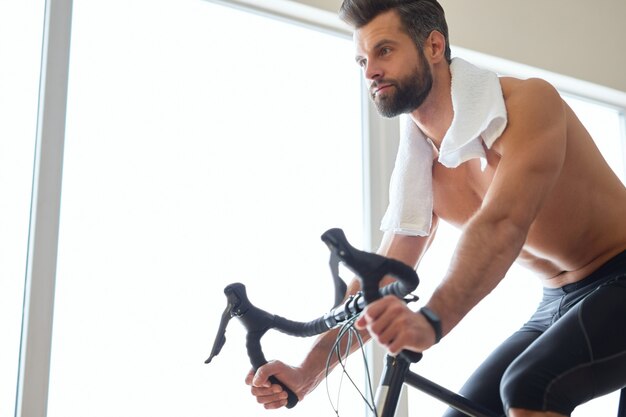 Apuesto joven con entrenador de bicicleta en casa