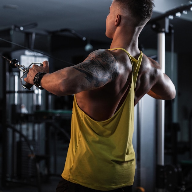 Un apuesto joven entrenador fuerte con una espalda musculosa hace ejercicio en el gimnasio