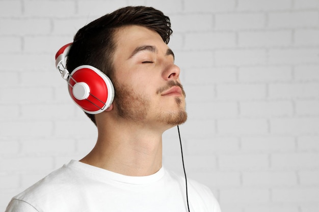 Apuesto joven escuchando música sobre fondo de pared de ladrillo