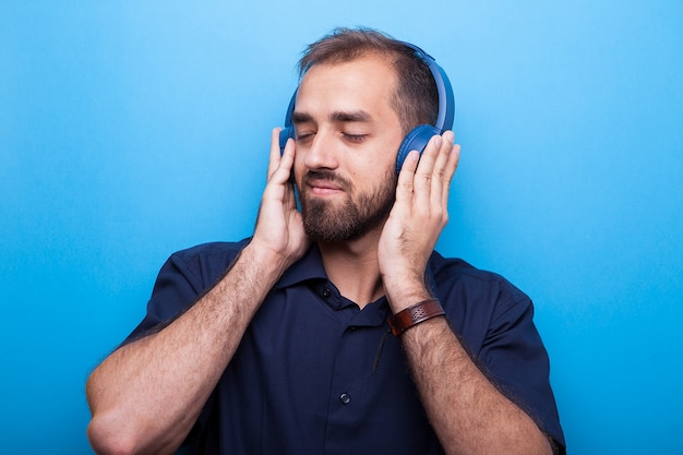 Apuesto joven escuchando música a través de auriculares sobre fondo azul.