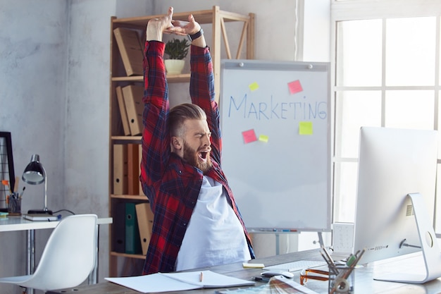 Apuesto joven estirando y bostezando después de un largo día de trabajo en su estudio creativo. Concepto de estilo de vida de oficina