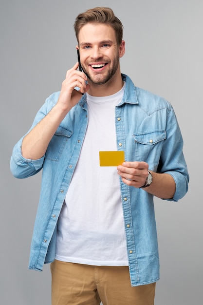 Apuesto joven feliz mostrando tarjeta de descuento de banco en blanco cor