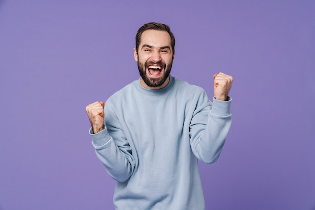 un apuesto joven feliz positivo aislado sobre una pared púrpura que muestra el gesto del ganador.