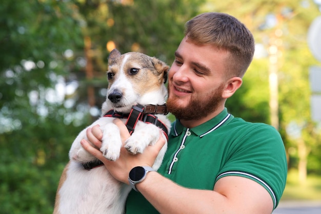 Un apuesto joven feliz sosteniendo a su mascota un hermoso perro en las manos sonríe al aire libre en el día soleado de verano