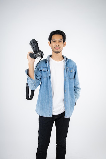 Un apuesto joven fotógrafo posa con una sonrisa y sostiene una cámara digital profesional en el estudio.