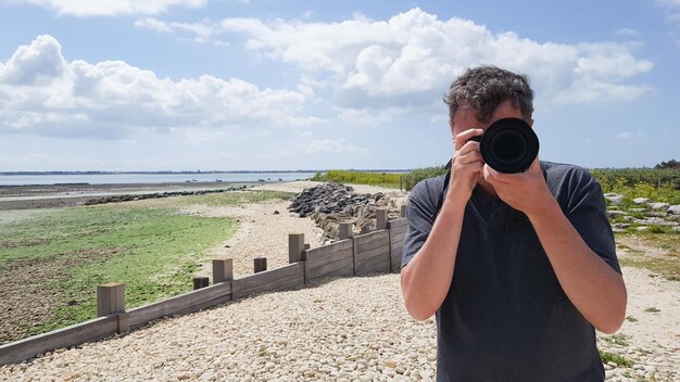 Apuesto joven fotógrafo profesional tomando fotos al aire libre en la costa de la playa junto al mar