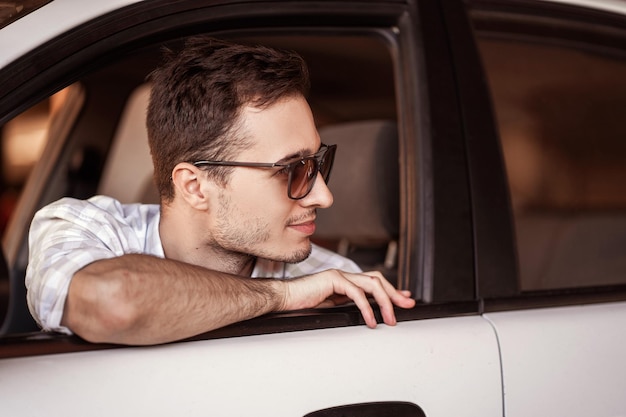 Apuesto joven con gafas en un coche blanco