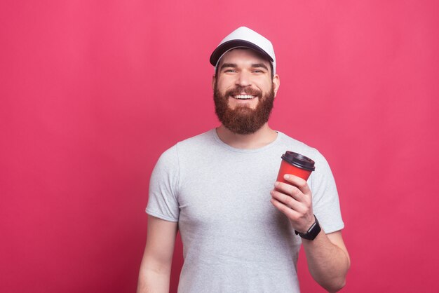 Apuesto joven con gorra sosteniendo una taza de café para ir sobre fondo rosa