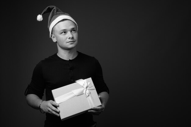 apuesto joven con gorro de Papá Noel listo para Navidad contra la pared gris. en blanco y negro