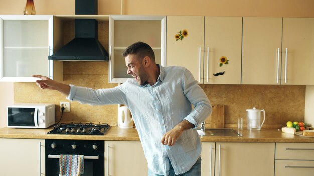 Apuesto joven gracioso bailando en la cocina en casa por la mañana y diviértete en las vacaciones