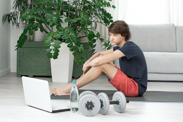 Apuesto joven hace deportes en casa en línea. Adolescente está entrenando en la habitación