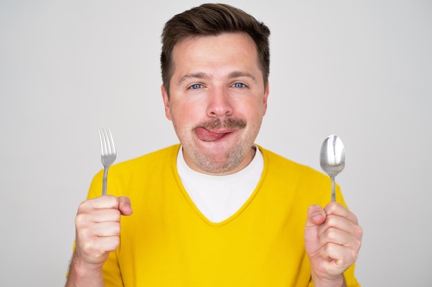 Apuesto joven hambriento sosteniendo tenedor y cuchara esperando la cena