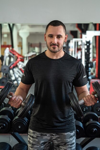 Apuesto joven con una hermosa figura trabaja como entrenador de fitness en un prestigioso gimnasio