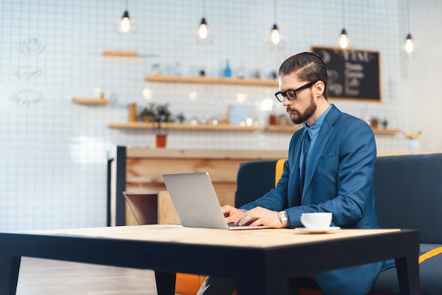 Un apuesto joven hombre de negocios con anteojos usando una laptop mientras bebe café en la cafetería