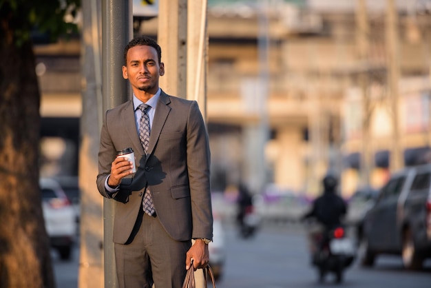 Apuesto joven hombre de negocios negro con traje en la calle de la ciudad mientras espera el transporte