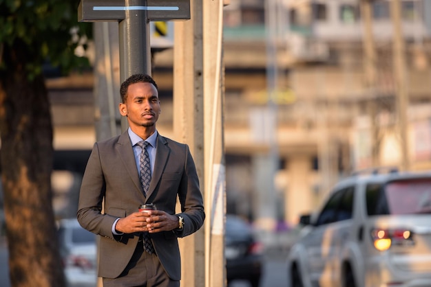 Apuesto joven hombre de negocios negro con traje en la calle de la ciudad mientras espera el transporte