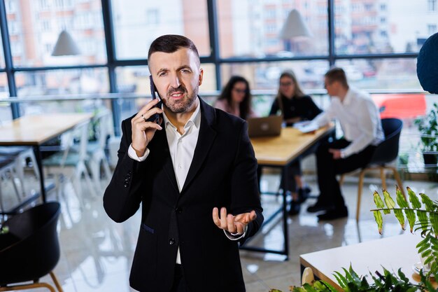 Un apuesto joven hombre de negocios con traje moderno usando su teléfono móvil, un hombre exitoso hablando por teléfono en la oficina