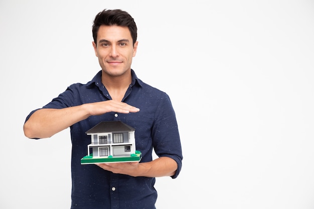 Foto apuesto joven inspector sosteniendo una sola casa, servicio de inspección de la casa antes de transferir al concepto de propietario de la casa