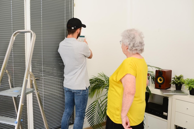 Apuesto joven instalando la seguridad de la casa cámara anti robo y alarma de sirena en una casa de mujer mayor