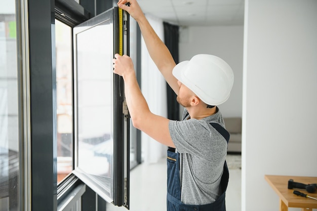 Apuesto joven instalando ventana salediza en el sitio de construcción de una casa nueva