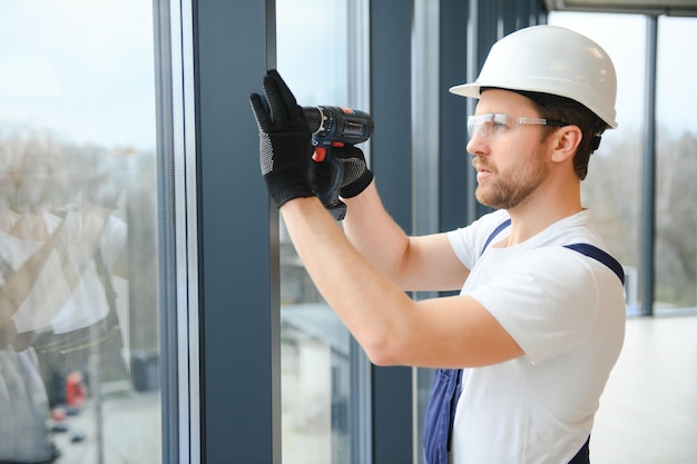 Foto apuesto joven instalando ventana salediza en el sitio de construcción de una casa nueva