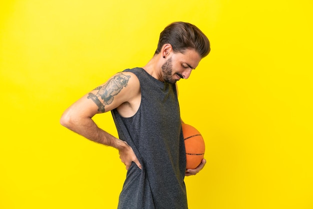 Apuesto joven jugador de baloncesto aislado de fondo amarillo que sufre de dolor de espalda por haber hecho un esfuerzo