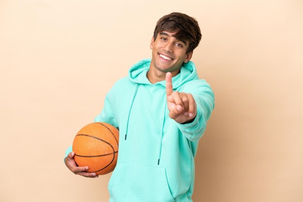 Apuesto joven jugador de baloncesto hombre aislado sobre fondo ocre mostrando y levantando un dedo