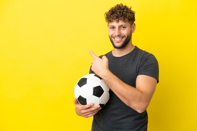 Apuesto joven jugador de fútbol hombre aislado sobre fondo amarillo apuntando hacia atrás