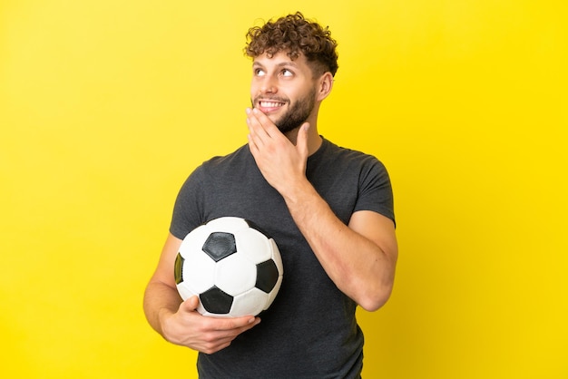 Apuesto joven jugador de fútbol hombre aislado sobre fondo amarillo mirando hacia arriba mientras sonríe