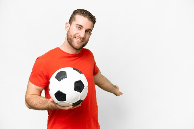 Apuesto joven jugador de fútbol sobre fondo blanco aislado extendiendo las manos a un lado para invitar a venir