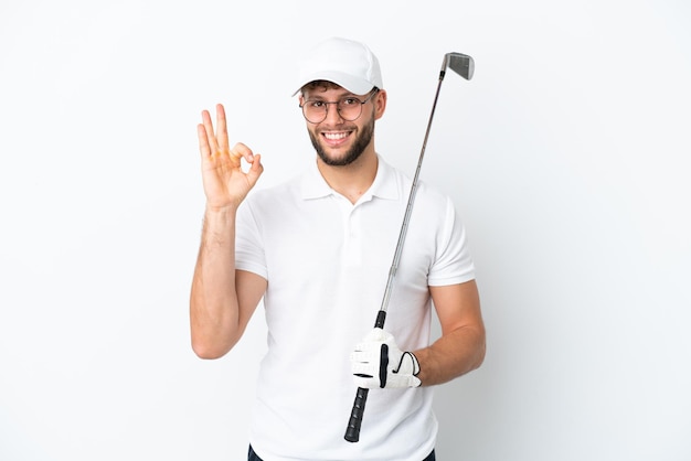 Apuesto joven jugando al golf aislado sobre fondo blanco mostrando signo ok con los dedos