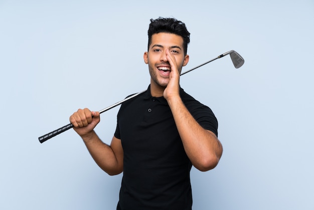 Apuesto joven jugando al golf sobre fondo azul aislado gritando con la boca abierta