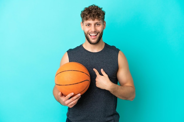 Apuesto joven jugando baloncesto aislado sobre fondo azul con expresión facial sorpresa