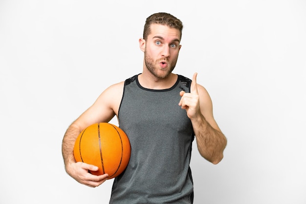 Apuesto joven jugando baloncesto sobre fondo blanco aislado con la intención de darse cuenta de la solución mientras levanta un dedo