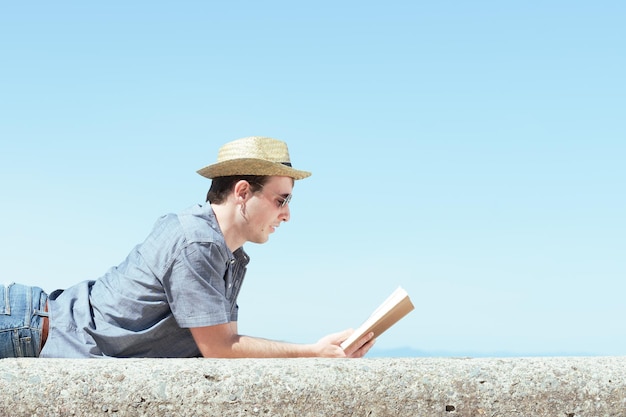 Apuesto joven leyendo un libro en un día soleado. Estudiar el concepto al aire libre.