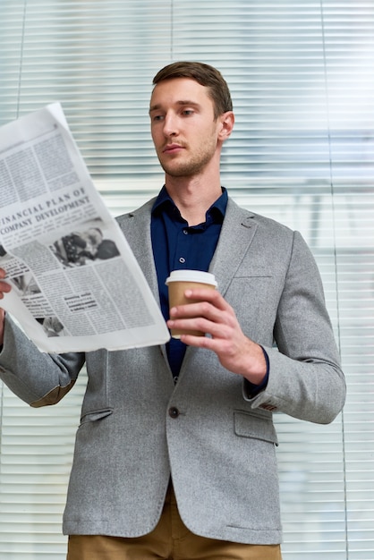 Apuesto joven leyendo el periódico en la oficina