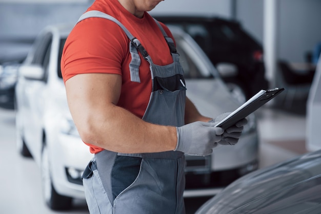 Apuesto joven mecánico de automóviles en uniforme está examinando el coche en auto servicio