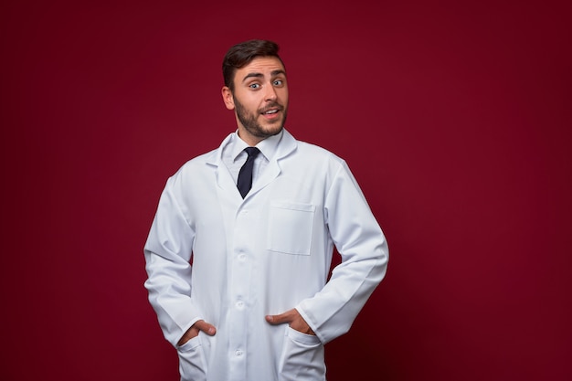 Foto apuesto joven médico caucásico adulto sobre fondo rojo. estudiante de medicina