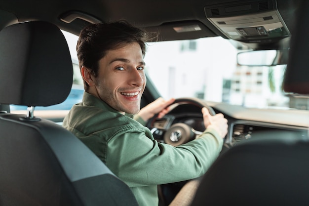 Apuesto joven mirando hacia atrás a la cámara sentado en el estacionamiento del automóvil vista automática desde el asiento trasero