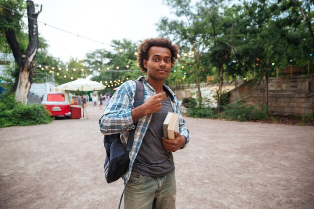 Apuesto joven con mochila y libros de pie al aire libre