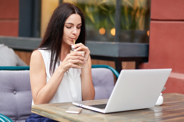 Apuesto joven modelo femenino bebe sabrosa bebida, concebido en la computadora portátil moderna