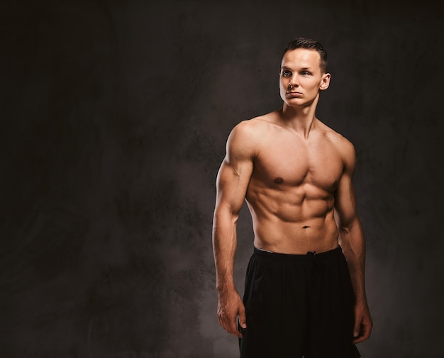 Un apuesto joven modelo de fitness con cuerpo musculoso posando en el estudio sobre un fondo oscuro.