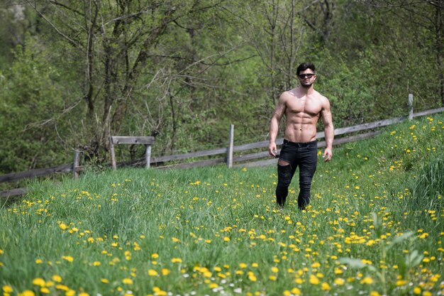 Apuesto joven modelo de pie fuerte al aire libre y flexionando los músculos Muscular culturista atlético hombre posando un lugar para su texto