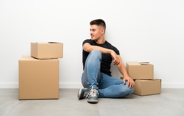 Apuesto joven moviéndose en una nueva casa entre cajas mirando hacia el lado