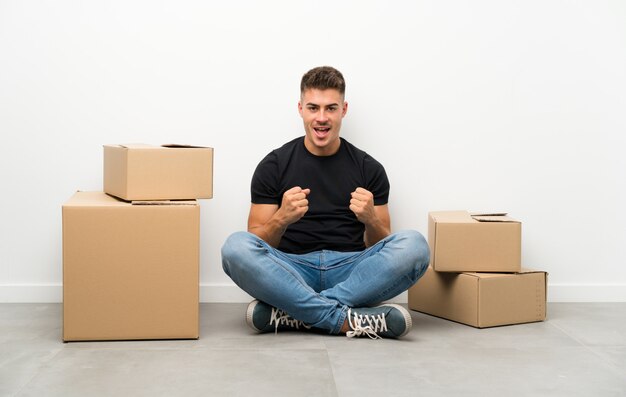 Apuesto joven moviéndose en un nuevo hogar entre cajas celebrando una victoria